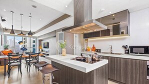 A modern kitchen with a central island, pendant lighting, and a large window providing natural light. - Jade by Kozystay - Kuningan (Jakarta)