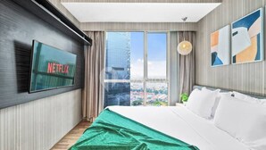 A modern hotel room with a large bed, a flat-screen TV mounted on the wall, and a city view through large windows. - Jade by Kozystay - Kuningan (Jakarta)