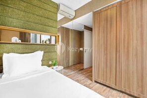 A modern hotel room with a bed, a small bedside table, a green textured wall, and a wooden wardrobe.