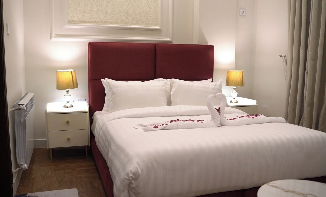 A neatly made bed with white linens, a red headboard, and two bedside lamps.