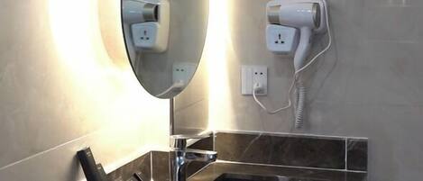 Un baño moderno con un lavabo de mármol, un espejo grande y un secador de pelo montado en la pared.