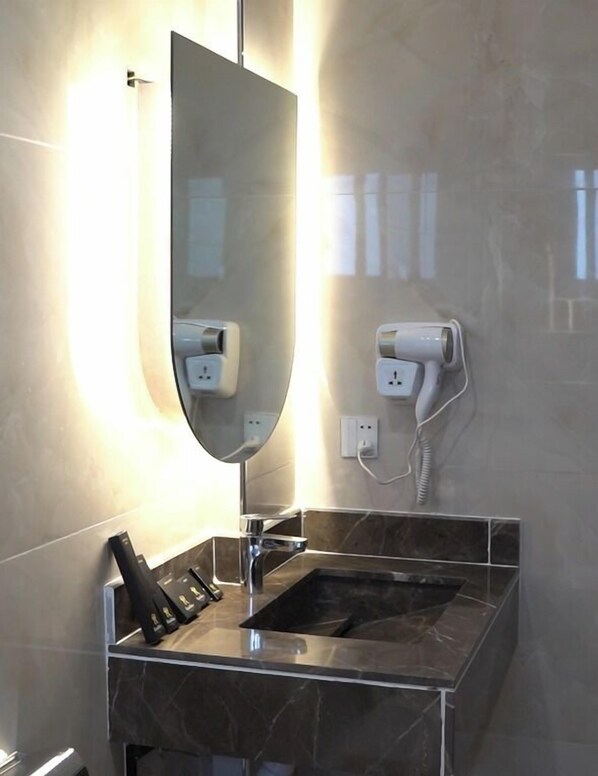 A modern bathroom with a marble sink, a large mirror, and a hairdryer mounted on the wall.