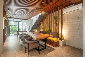 A modern interior with a wooden dining table, chairs, a staircase, and a seating area with cushions.