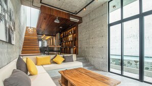 A modern interior with a wooden ceiling, a white sofa with cushions, a wooden coffee table, and large windows offering a view.