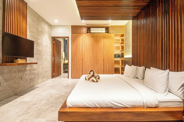 A modern bedroom with a large bed, wooden paneling, a flat-screen TV, and a built-in shelf.