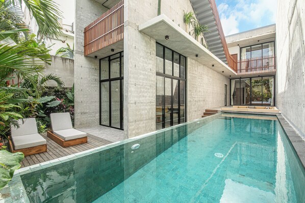 A modern outdoor pool area with a concrete deck, lounge chairs, and a clear blue pool.