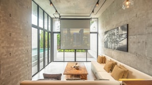A modern living room with a large window, a wooden coffee table, a sofa, and a cityscape view.