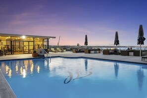 A rooftop pool area with lounge chairs and umbrellas, a fitness center, and a view of the city skyline.