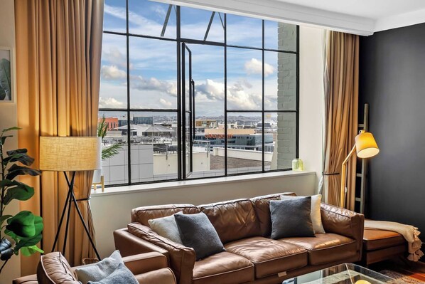 A room with a large window, a leather sofa, a floor lamp, and a plant.