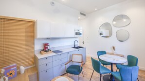 A modern kitchen with white cabinets, a built-in oven, and a sink. There is a dining area with a round table and blue chairs. - Villa Victor Hugo by Odomo (Avignon)