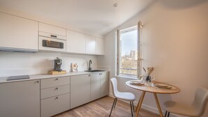A modern kitchen with white cabinets, a built-in oven, and a dining area with a round table and two chairs. - Villa Victor Hugo by Odomo (Avignon)