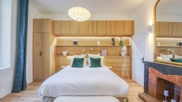 A modern bedroom with a large bed, wooden headboard, bedside tables, a mirror, and a fireplace.