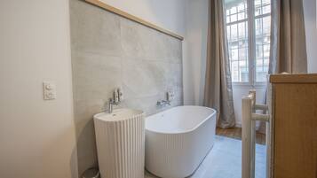 A modern bathroom with a freestanding bathtub, a pedestal sink, and a large window with curtains.