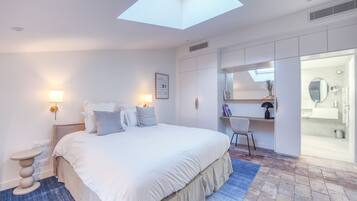 Une chambre moderne avec une lucarne, un grand lit, des lampes de chevet, un bureau et une salle de bain équipée d’un miroir et d’un lavabo.