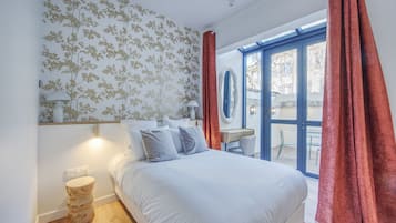Ein Schlafzimmer mit einem Bett, einem Nachttisch, einem Spiegel und einem Fenster mit Vorhängen.