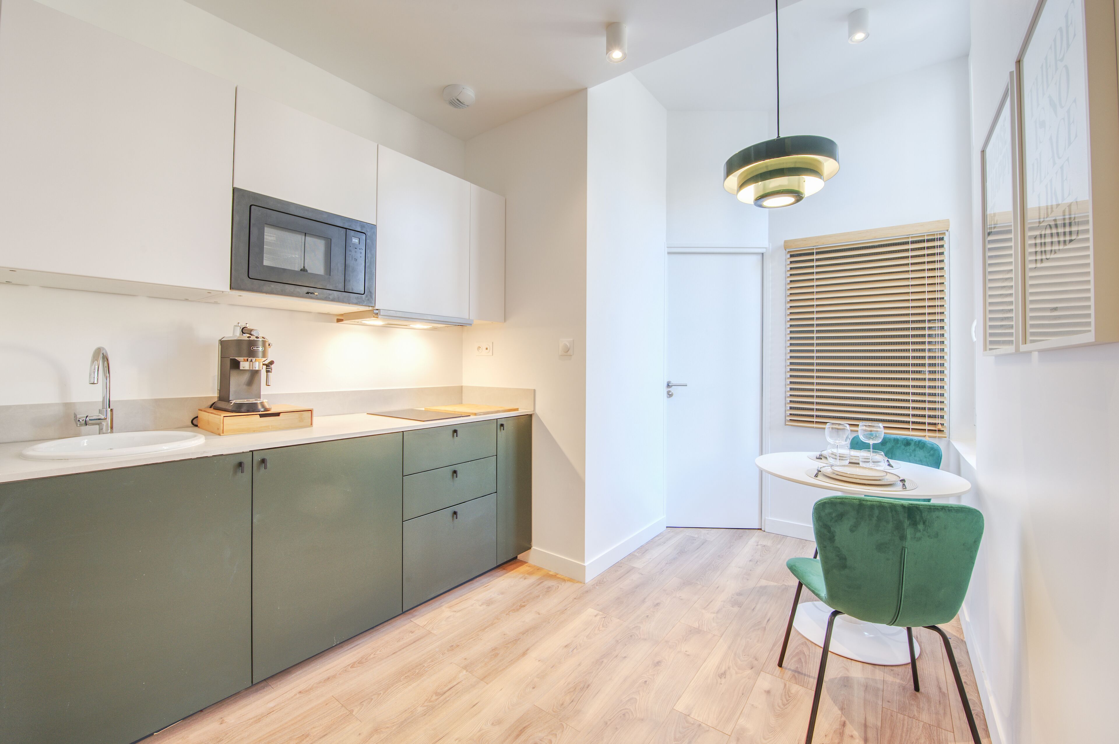 A modern kitchen with a microwave, sink, and green cabinets. There is a dining area with a table and chairs.