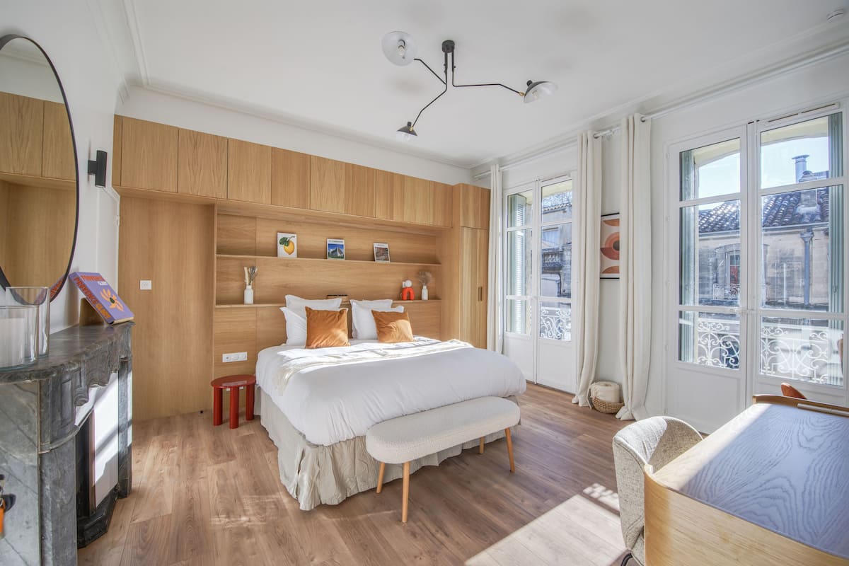 A bedroom with a wooden wardrobe, a bed with white bedding, a bench, and a bedside table.
