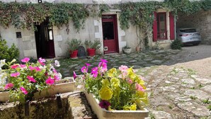 A stone building with red doors and windows, potted plants, and a parked car.
