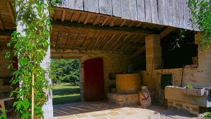 A rustic stone building with a wooden roof, a red door, and a stone floor.