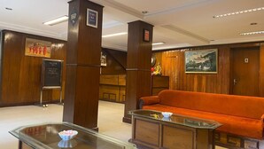 A lobby with a wooden reception desk, a glass-top table with a bowl, and an orange sofa. - Orangepetal Comfort Himalayan Resort (Darjeeling)
