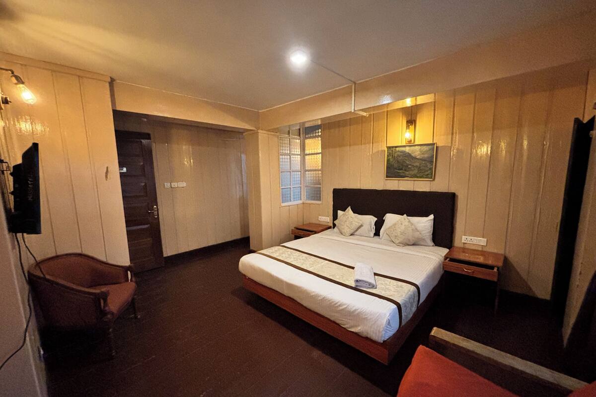 Habitación de hotel con una cama grande, una silla, una mesita y un televisor montado en la pared.