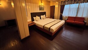 A hotel room with a large bed, a wooden nightstand, a red sofa, and a window with curtains. - Orangepetal Comfort Himalayan Resort (Darjeeling)