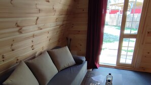 Una habitación acogedora con detalles de madera, un sofá con cojines, una mesa de centro con posavasos y una ventana con cortinas.