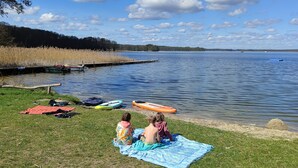 Escena junto a un lago con dos niños sobre una manta, barcos y un muelle.