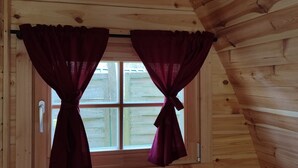 Habitación de cabaña de madera con ventana y dos cortinas atadas en la parte superior.