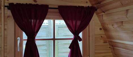 A wooden cabin room with a window featuring two curtains tied at the top.