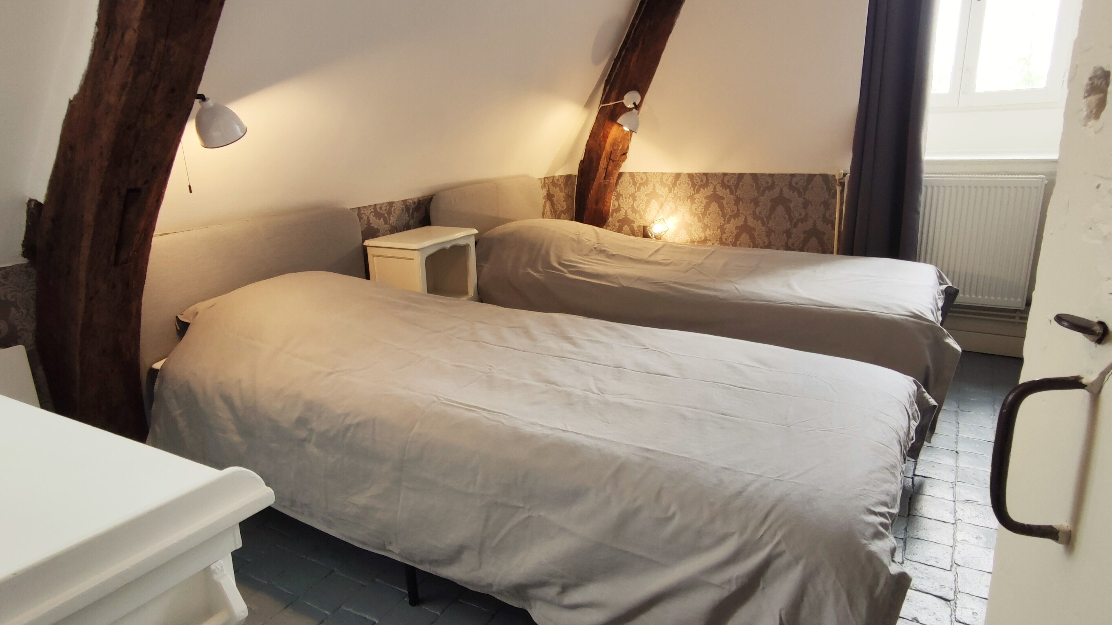 A room with two beds, a small bedside table, a lamp, and a radiator.