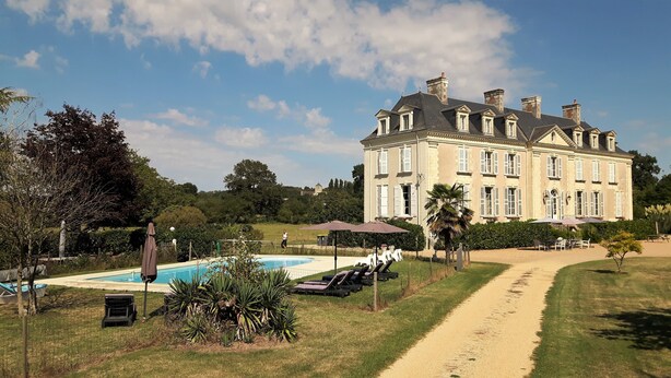 A large, historic building with a swimming pool and sun loungers.
