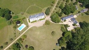 An aerial view of a large estate with a main building, a swimming pool, and surrounding greenery.
