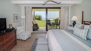 Un dormitorio con una cama, un televisor, un aparador de madera y vistas a la playa a través de una puerta corrediza de vidrio.