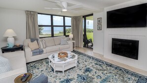 Una sala de estar con sofá, mesa de centro y chimenea. Hay un ventanal con vistas al océano.