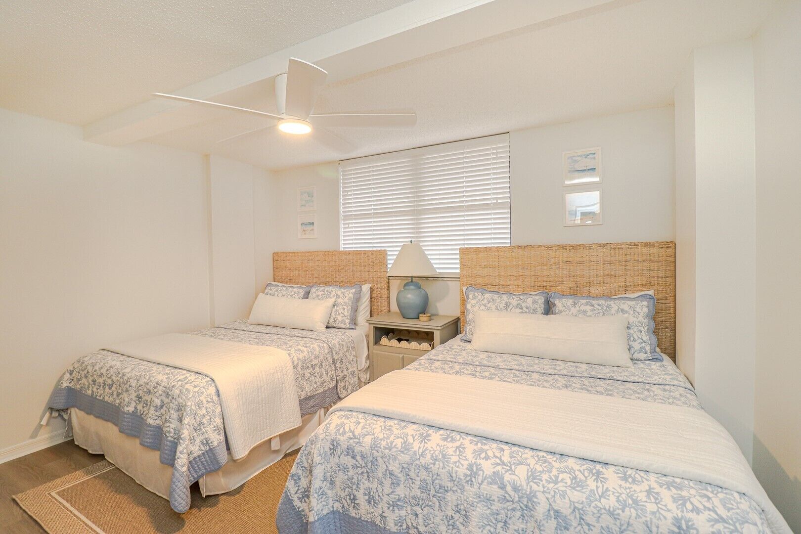 Een slaapkamer met twee bedden, een plafondventilator en een raam met jaloezieën.