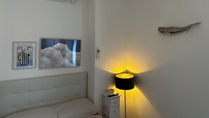 A bedroom with a bed, a bedside table, a lamp, an air conditioner, and wall art. - Cosy Studio Near Rapallo Beach Via Baisi (Rapallo)