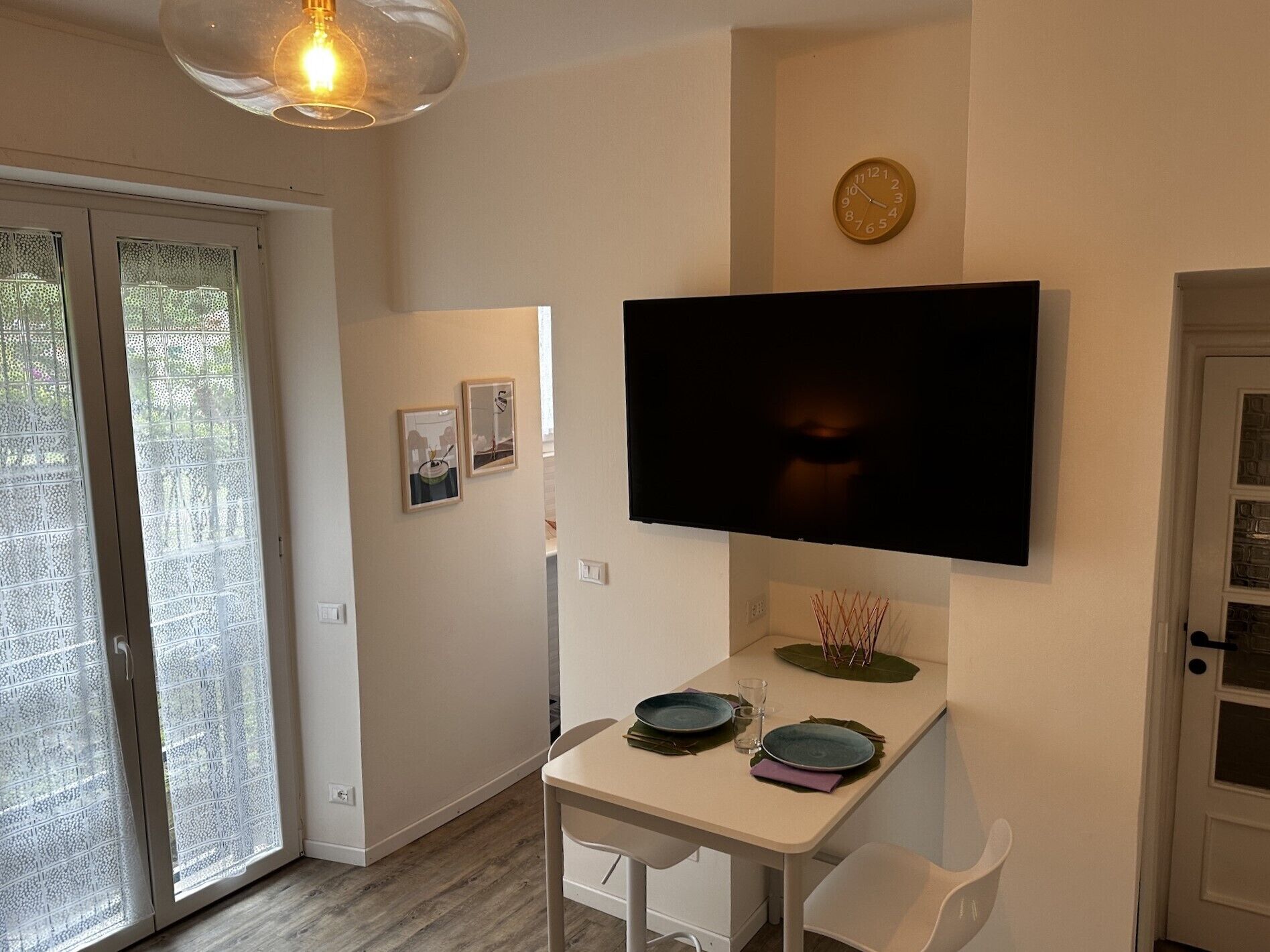 En matplats med ett bord dukat för två personer, en väggmonterad TV och en dörr med frostat glas.