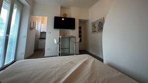 A bedroom with a bed, a TV mounted on the wall, a small table with chairs, and a kitchen area visible through an open door. - Cosy Studio Near Rapallo Beach Via Baisi (Rapallo)
