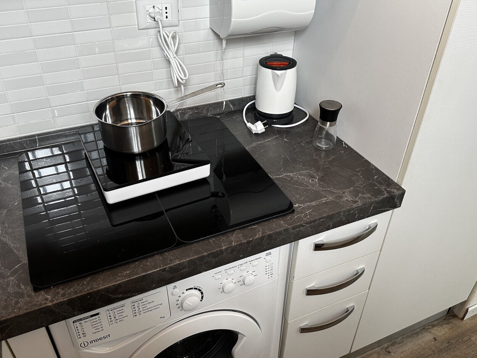 A kitchen with a black countertop, a stainless steel pot, a coffee maker, and a washing machine.