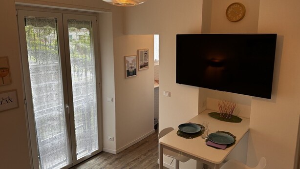 A dining area with a table set for two, a television mounted on the wall, and a sliding glass door leading to an outdoor area. - Cosy Studio Near Rapallo Beach Via Baisi (Rapallo)