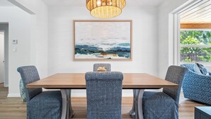 A dining area with a wooden table and patterned chairs, a woven light fixture, and a landscape painting on the wall. - Villa Azul | Pool + Guest House | Northwood Hills (West Palm Beach)