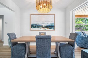 A dining area with a wooden table and patterned chairs, a woven light fixture, and a landscape painting on the wall. - Villa Azul | Pool + Guest House | Northwood Hills (West Palm Beach)