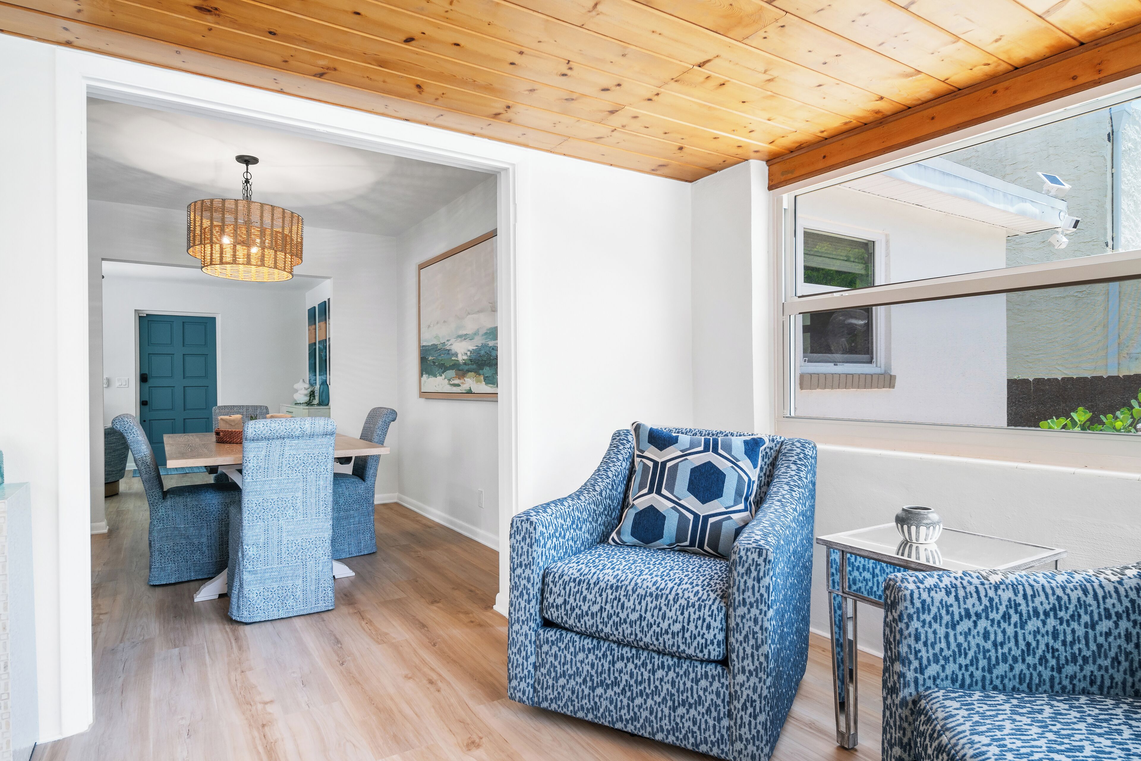 Un intérieur moderne comprenant un coin repas, un espace salon avec des fauteuils à motifs, un plafond en bois et une grande fenêtre.