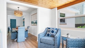 Un intérieur moderne comprenant un coin repas, un espace salon avec des fauteuils à motifs, un plafond en bois et une grande fenêtre.