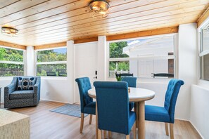 Una habitación con techo de madera, una mesa redonda con cuatro sillas y un sillón estampado.