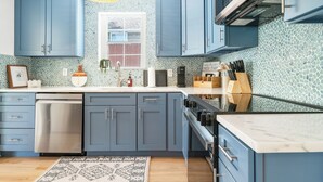 A kitchen with blue cabinets, a stainless steel dishwasher, and a tiled backsplash. - Villa Azul | Pool + Guest House | Northwood Hills (West Palm Beach)