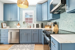 A kitchen with blue cabinets, a stainless steel dishwasher, and a tiled backsplash. - Villa Azul | Pool + Guest House | Northwood Hills (West Palm Beach)