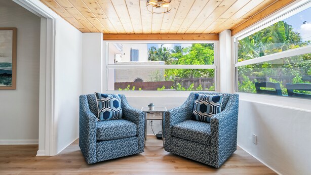 A room with a wooden ceiling, two patterned armchairs, a small table, and a view of greenery outside. - Villa Azul | Pool + Guest House | Northwood Hills (West Palm Beach)