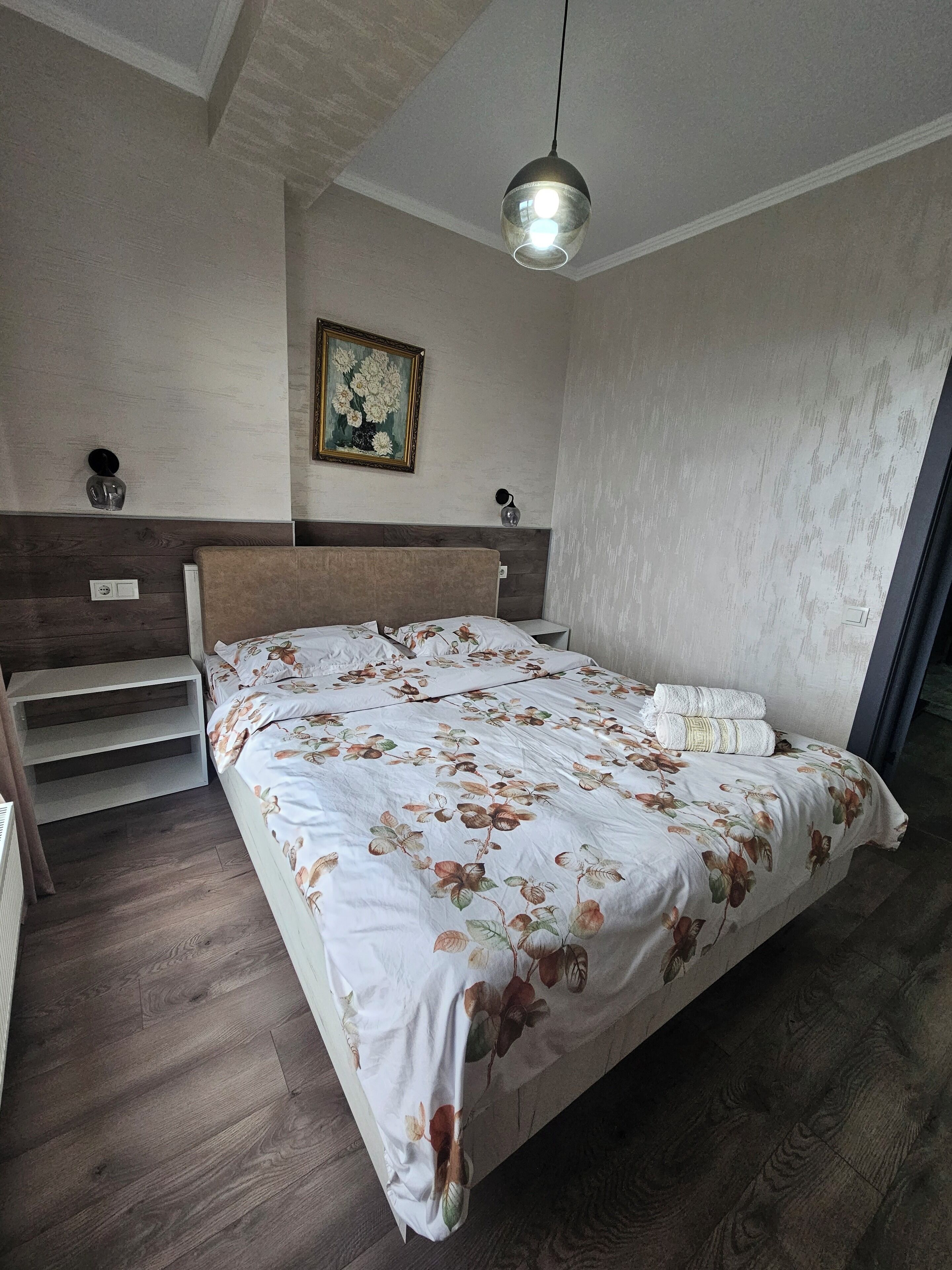 Une chambre à coucher avec un grand lit, une table de chevet, une lampe fixée au mur et un tableau.